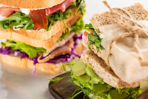 Selective focus of fresh sandwiches with meat on wooden cutting board on white surface — Stock Photo