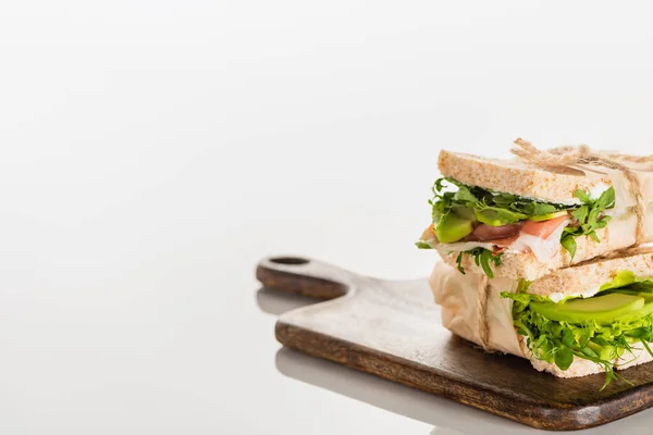 Selektiver Schwerpunkt frischer grüner Sandwiches mit Avocado und Fleisch auf Holzschneidebrett auf weißer Oberfläche — Stockfoto