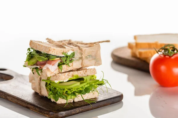 Foco seletivo de sanduíches verdes frescos com abacate e carne em placa de corte de madeira na superfície branca — Fotografia de Stock
