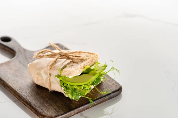 Fresh green vegan sandwich with avocado on wooden cutting board on white marble surface — Stock Photo