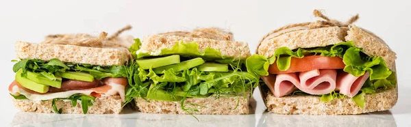 Fresh green sandwiches with avocado and meat on white surface, panoramic shot — Stock Photo