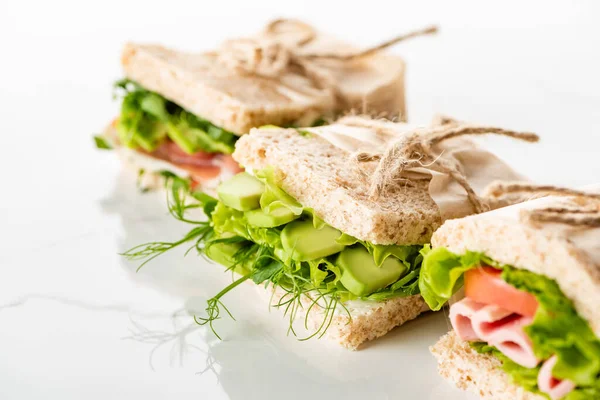 Selektiver Schwerpunkt frischer grüner Sandwiches mit Avocado und Fleisch auf weißer Oberfläche — Stockfoto