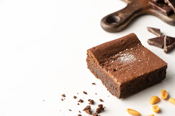 Délicieux morceau de brownie près de noix et chocolat sur fond blanc — Photo de stock