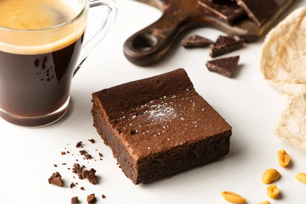 Foco seletivo de delicioso pedaço de brownie perto de café no fundo branco — Fotografia de Stock