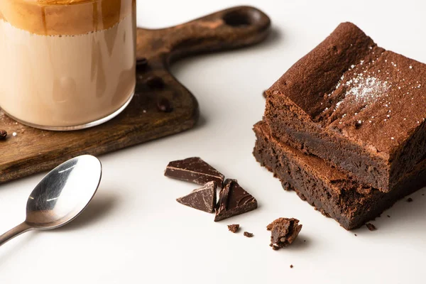 Köstliche Brownie-Stücke in der Nähe von Holz Schneidebrett mit Kaffee und Löffel auf weißem Hintergrund — Stockfoto