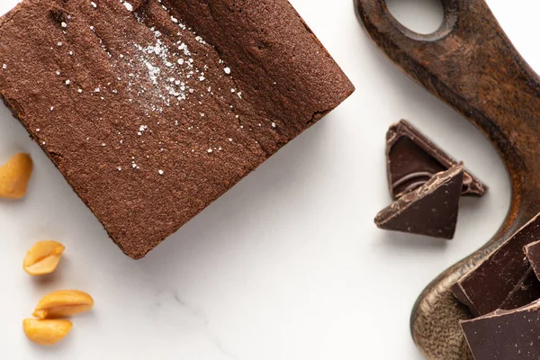 Vue du dessus de délicieux morceau de brownie près de la planche à découper en bois, noix et chocolat sur fond blanc — Photo de stock