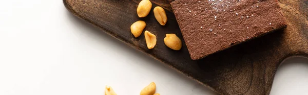 Top view of delicious brownie piece on wooden cutting board with nuts on white background, panoramic shot — Stock Photo