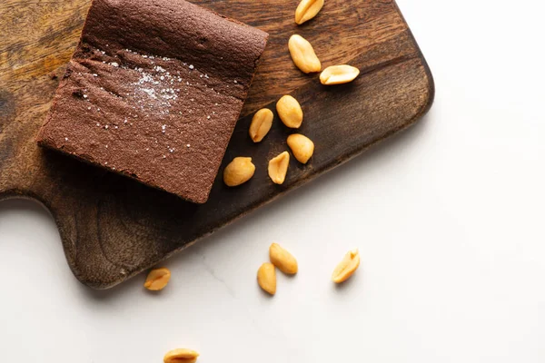 Top view of delicious brownie piece on wooden cutting board with nuts on white background — Stock Photo