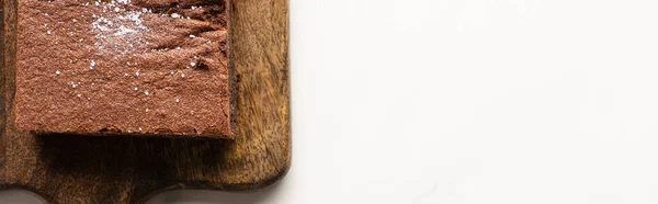 Top view of delicious brownie piece on wooden cutting board on white background, panoramic shot — Stock Photo