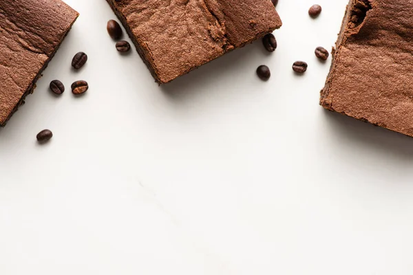 Vista superior de deliciosos pedaços de brownie com grãos de café no fundo branco — Fotografia de Stock