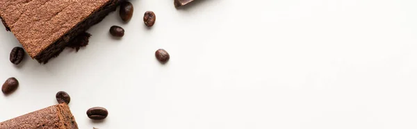 Vista superior de deliciosas piezas de brownie con granos de café sobre fondo blanco, plano panorámico - foto de stock