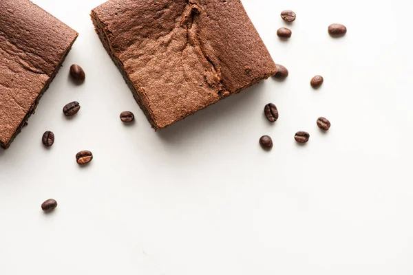 Vue de dessus de délicieux morceaux de brownie avec des grains de café sur fond blanc — Photo de stock