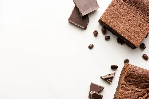 Vue du dessus de délicieux morceaux de brownie avec des grains de café et du chocolat sur fond blanc — Photo de stock