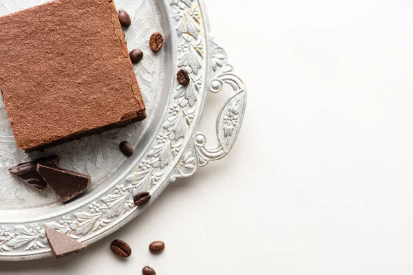 Top view of delicious brownie piece with coffee beans and chocolate on silver tray on white background — Stock Photo