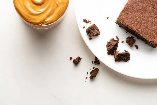 Top view of delicious brownie piece on plate near peanut butter on white background — Stock Photo