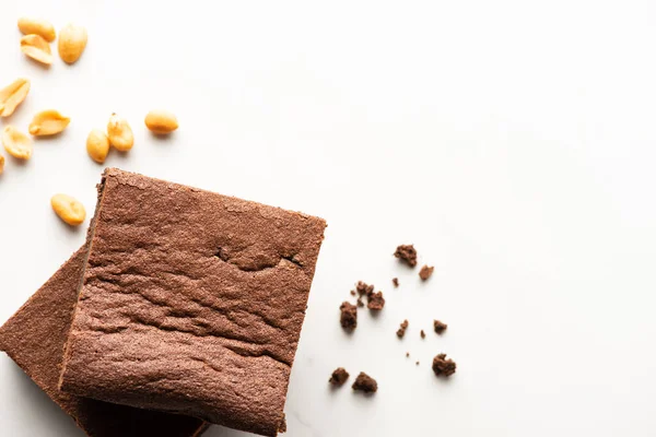 Top view of delicious brownie pieces and peanuts on white background — Stock Photo