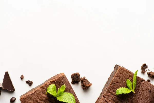 Vista dall'alto di deliziosi pezzi di brownie con menta e cioccolato su sfondo bianco — Foto stock