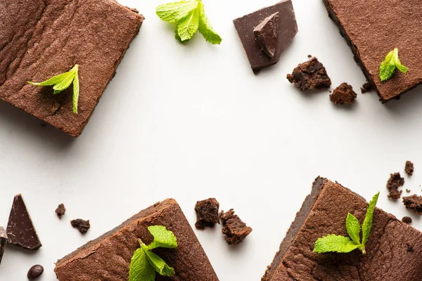 Vista dall'alto di deliziosi pezzi di brownie con menta e cioccolato su sfondo bianco — Foto stock