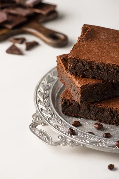 Messa a fuoco selettiva di deliziosi pezzi di brownie su vassoio d'argento con chicchi di caffè su sfondo bianco — Foto stock