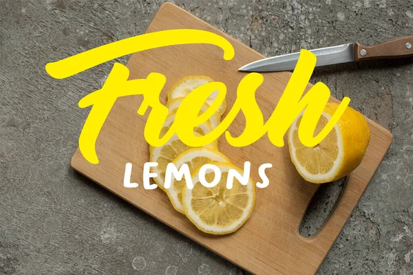 Vista dall'alto di limone tagliato a fette su tagliere in legno con coltello su superficie di cemento grigio, illustrazione di limoni freschi — Foto stock