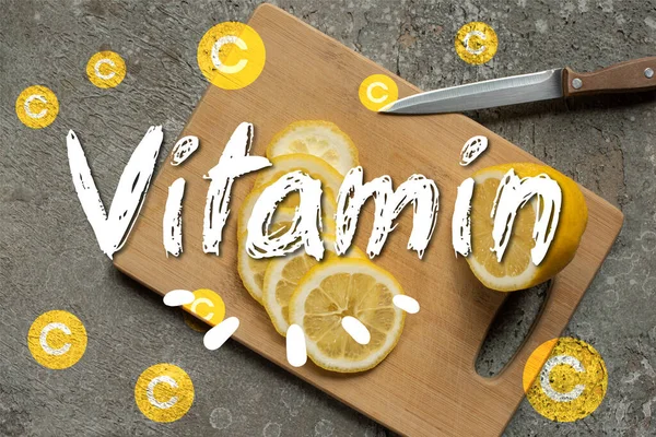 Vista superior de limón en rodajas sobre tabla de cortar de madera con cuchillo sobre superficie de hormigón gris, ilustración de vitaminas - foto de stock