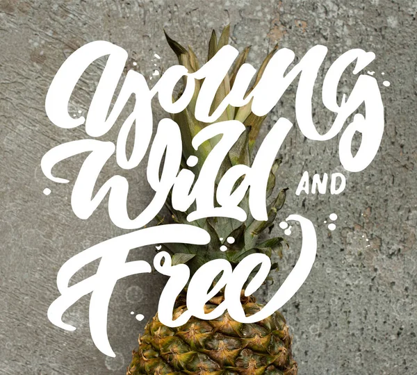 Top view of ripe pineapple on grey concrete surface with young, wild and free illustration — Stock Photo