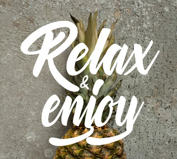 Top view of ripe pineapple on grey concrete surface with relax and enjoy illustration — Stock Photo