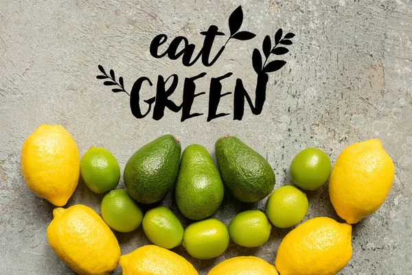 Vue de dessus de l'avocat coloré, les citrons verts et les citrons sur la surface en béton gris avec manger illustration verte — Photo de stock