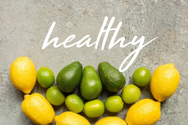 Вид сверху на красочный авокадо, лаймы и лимоны на серой бетонной поверхности, здоровая иллюстрация — стоковое фото