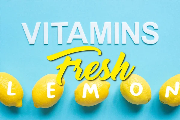 Vista superior de limones amarillos maduros y vitaminas de la palabra sobre fondo azul, ilustración fresca - foto de stock