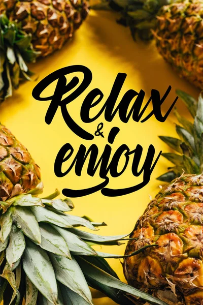 Selective focus of fresh ripe pineapples with green leaves on yellow background with relax and enjoy illustration — Stock Photo