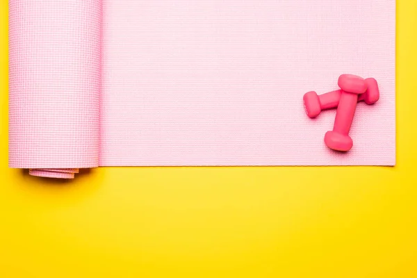 Vue de dessus du tapis de fitness rose et des haltères sur fond jaune — Photo de stock