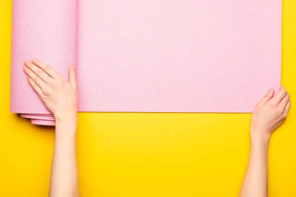 Cropped view of woman rolling out pink fitness mat on yellow background — Stock Photo