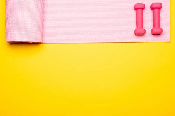 Flat lay with pink fitness mat and dumbbells on yellow background — Stock Photo