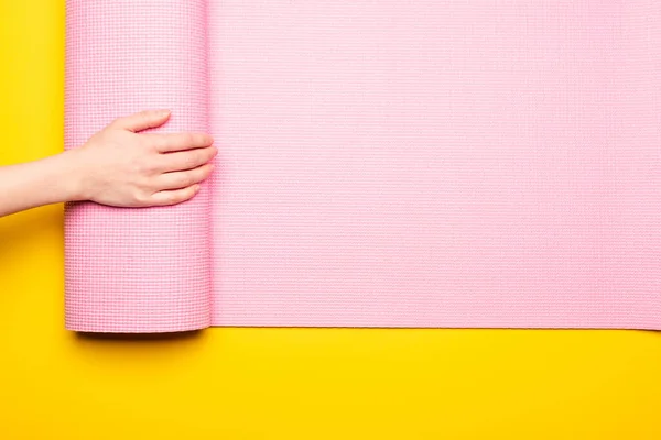 Vista recortada de la mujer desplegando alfombra de fitness rosa sobre fondo amarillo - foto de stock