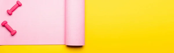 Top view of pink fitness mat and dumbbells on yellow background, panoramic shot — Stock Photo