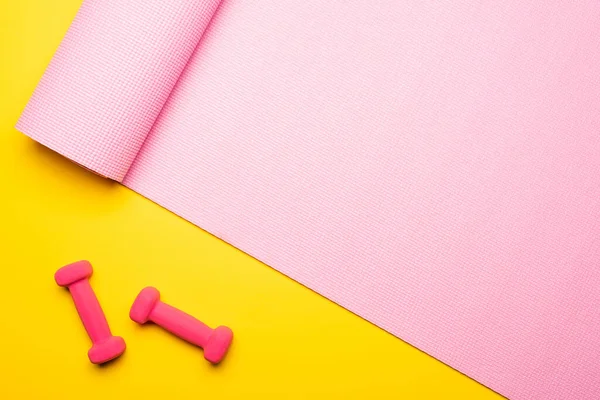 Vue de dessus du tapis de fitness rose et des haltères sur fond jaune — Photo de stock