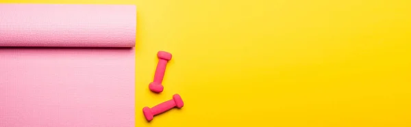 Top view of pink fitness mat and dumbbells on yellow background, panoramic shot — Stock Photo