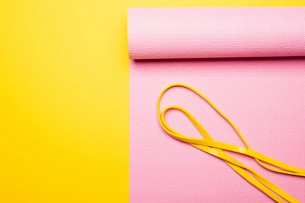 Vista superior de la banda elástica en la esterilla de fitness rosa sobre fondo amarillo - foto de stock