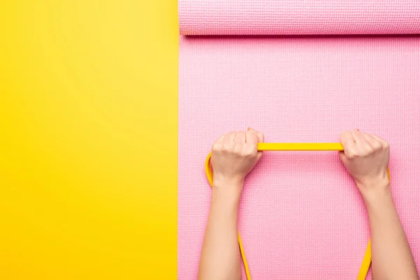 Cropped view of woman holding elastic band on pink fitness mat on yellow background — Stock Photo