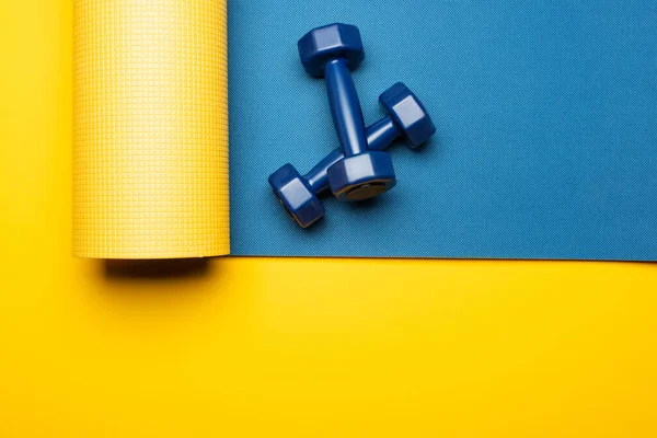 Vista superior de la alfombra de fitness azul con mancuernas sobre fondo amarillo - foto de stock