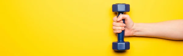 Cropped view of woman holding blue dumbbell on yellow background, panoramic shot — Stock Photo