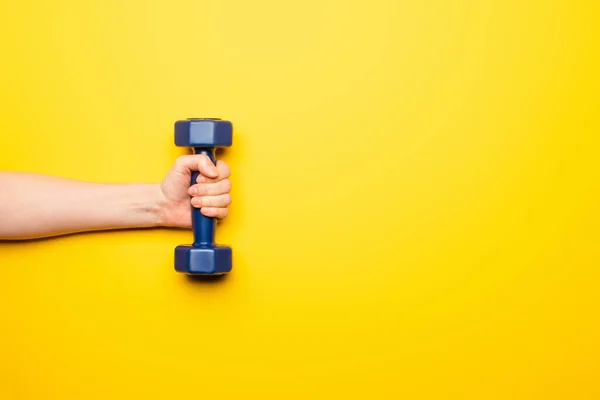 Cropped view of woman holding blue dumbbell on yellow background — Stock Photo