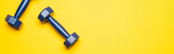 Top view of blue dumbbells on yellow background, panoramic shot — Stock Photo