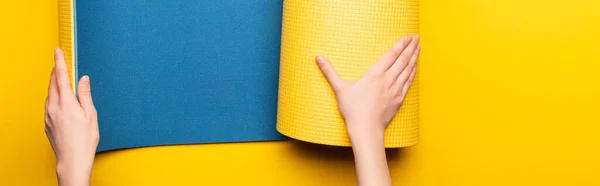 Visão parcial da mulher rolando tapete de fitness azul no fundo amarelo, tiro panorâmico — Fotografia de Stock