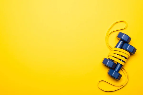 Top view of blue dumbbells in resistance band on yellow background — Stock Photo