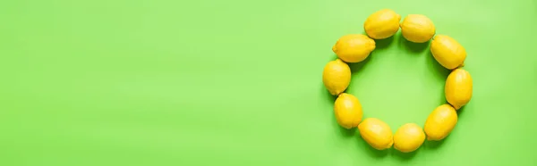 Vista superior de limones amarillos maduros dispuestos en marco redondo vacío sobre fondo verde, orientación panorámica - foto de stock