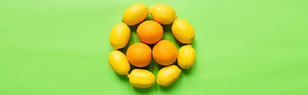 Top view of ripe lemons and oranges arranged in circle on green background, panoramic orientation — Stock Photo