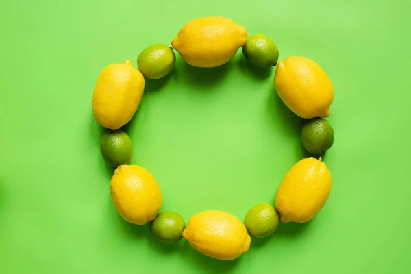 Top view of ripe lemons and limes arranged in round empty frame on green background — Stock Photo