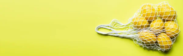 Top view of ripe whole lemons in string bag on yellow background, panoramic crop — Stock Photo